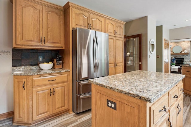 936 Broken Bow Ct, Delafield, WI 53018 - kitchen featuring freestanding refrigerator, decorative backsplash, light stone countertops, a center island, and light wood finished floors