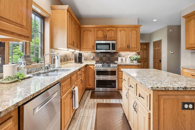 936 Broken Bow Ct, Delafield, WI 53018 - kitchen featuring stainless steel appliances, a sink, light stone counters, backsplash, and a kitchen island