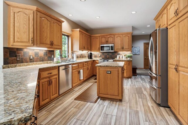 936 Broken Bow Ct, Delafield, WI 53018 - kitchen featuring stainless steel appliances, a center island, a sink, backsplash, and light stone countertops