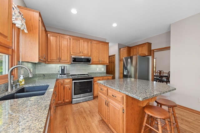 N66W13568 Crestwood Dr, Menomonee Falls, WI 53051 - kitchen featuring stainless steel appliances, a sink, light wood-style floors, a breakfast bar area, and light stone counters
