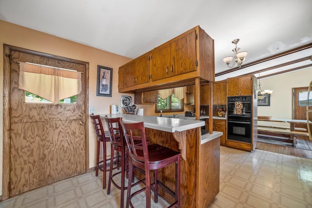 1104 Cavalier Dr, Waukesha, WI 53186 - kitchen featuring light floors, a chandelier, brown cabinetry, light countertops, and plenty of natural light