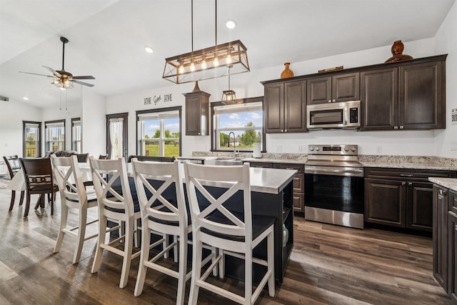 3815 Stone Wall Dr, De Pere, WI 54115 - kitchen with appliances with stainless steel finishes, a kitchen island, dark wood finished floors, dark brown cabinets, and recessed lighting