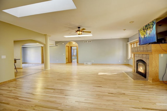 508 Frost Woods Rd, Monona, WI 53716 - unfurnished living room with arched walkways, light wood-style floors, a tile fireplace, a skylight, and ceiling fan