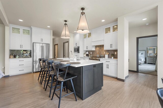 3812 Hawk Ledge Cir, De Pere, WI 54115 - kitchen with appliances with stainless steel finishes, backsplash, light wood finished floors, a breakfast bar, and a kitchen island with sink