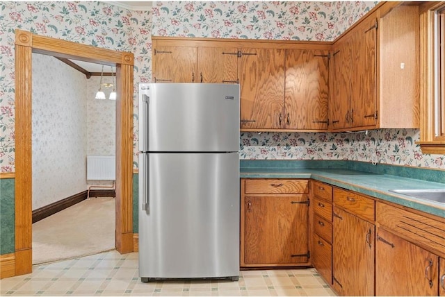 632 E 2nd St, New Richmond, WI 54017 - kitchen featuring freestanding refrigerator, wallpapered walls, brown cabinets, light flooring, and radiator heating unit
