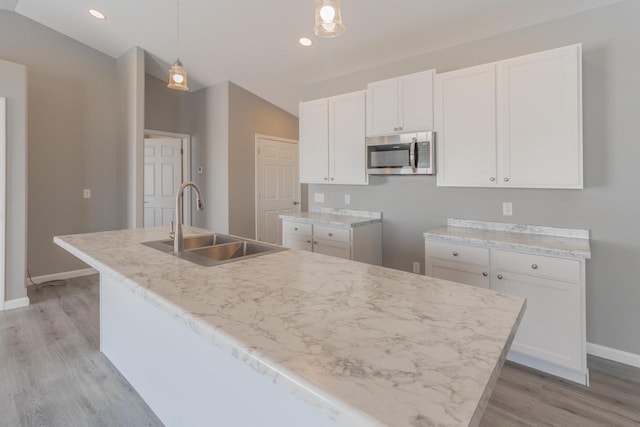 6308 Perch Dr, Weston, WI 54476 - kitchen with stainless steel microwave, light wood-type flooring, white cabinets, an island with sink, and pendant lighting