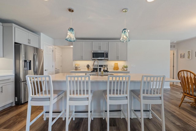 35209 Winnebago Ct, Summit, WI 53066 - kitchen with appliances with stainless steel finishes, light countertops, dark wood finished floors, an island with sink, and hanging light fixtures