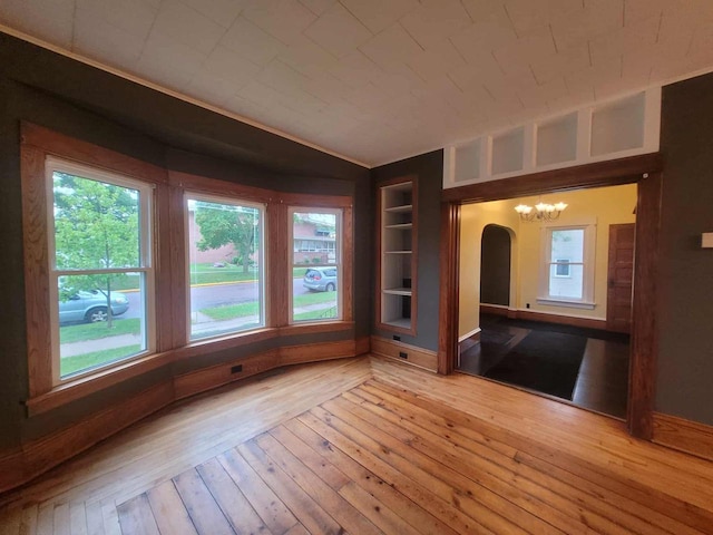 324 N Pine St, Reedsburg, WI 53959 - unfurnished room featuring a chandelier, built in shelves, arched walkways, light wood-style flooring, and baseboards