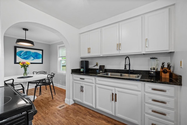 841 4th St S, Wisconsin Rapids, WI 54494 - kitchen featuring a sink, arched walkways, crown molding, white cabinetry, and light wood-style flooring