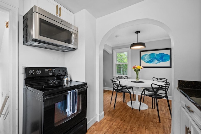 841 4th St S, Wisconsin Rapids, WI 54494 - kitchen featuring black range with electric stovetop, stainless steel microwave, arched walkways, white cabinets, and light wood finished floors