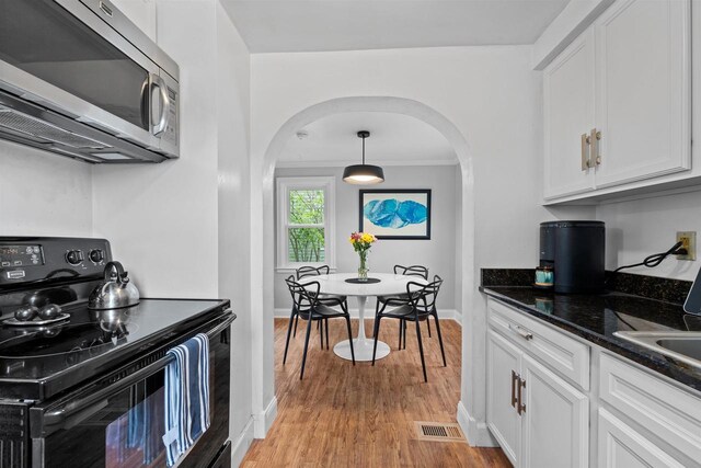 841 4th St S, Wisconsin Rapids, WI 54494 - kitchen with stainless steel microwave, black electric range, arched walkways, light wood-type flooring, and white cabinets