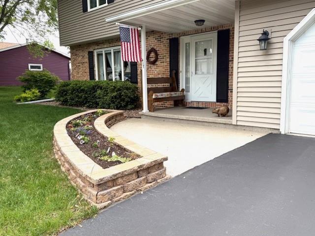 417 Raintree Dr, Fort Atkinson, WI 53538 - entrance to property with brick siding, a yard, a garage, and a porch