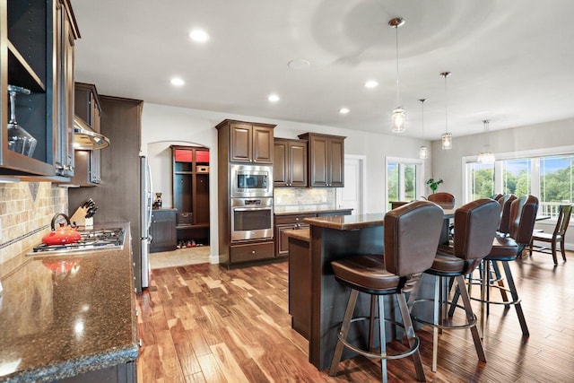 3403 Whistling Wind Way, Sun Prairie, WI 53590 - kitchen featuring appliances with stainless steel finishes, arched walkways, a kitchen breakfast bar, a center island, and tasteful backsplash