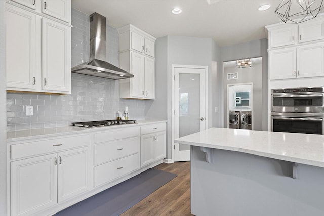 1279 E Hickory Creek Ct, Oak Creek, WI 53154 - kitchen with washing machine and clothes dryer, wall chimney exhaust hood, appliances with stainless steel finishes, dark wood finished floors, and backsplash