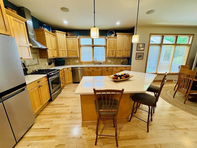 2659 Dungarvan Rd, Fitchburg, WI 53711 - kitchen with stainless steel appliances, wall chimney exhaust hood, light wood-type flooring, light countertops, and a kitchen bar