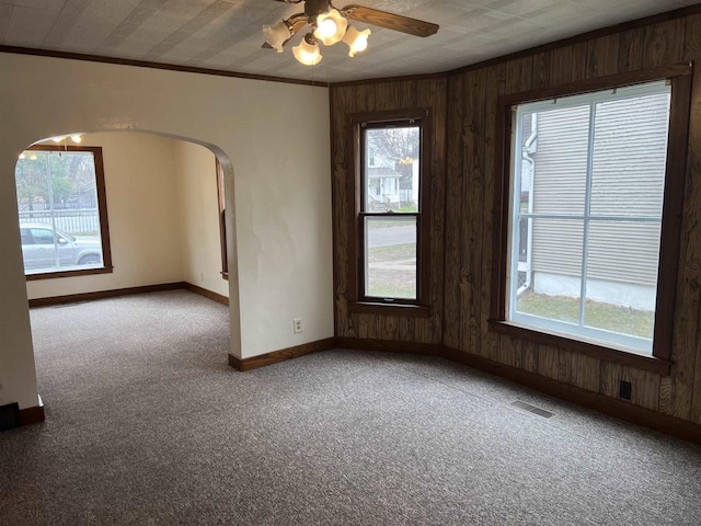 856 8th St, Beloit, WI 53511 - carpeted spare room featuring baseboards, wood walls, arched walkways, ceiling fan, and crown molding