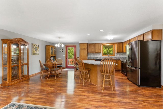9432 James Ave, Sparta, WI 54656 - kitchen with stainless steel appliances, dark wood-style floors, brown cabinetry, a kitchen bar, and backsplash