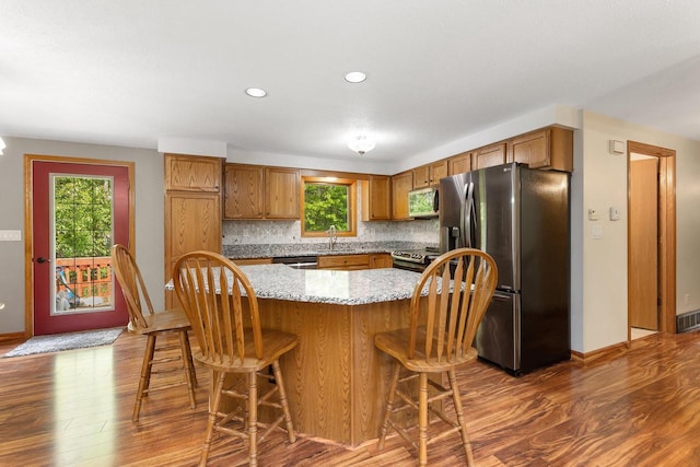 9432 James Ave, Sparta, WI 54656 - kitchen with stainless steel appliances, dark wood finished floors, a sink, a kitchen breakfast bar, and brown cabinetry