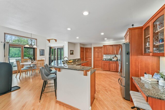 1441 W County Line Rd, River Hills, WI 53217 - kitchen with freestanding refrigerator, a kitchen bar, brown cabinetry, glass insert cabinets, and dark stone counters
