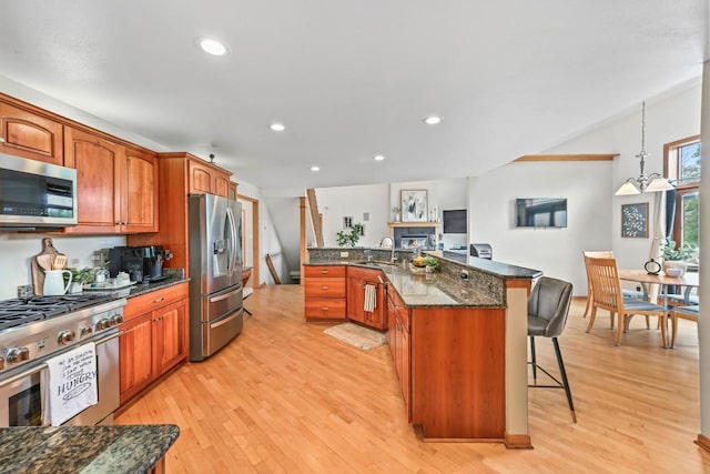 1441 W County Line Rd, River Hills, WI 53217 - kitchen featuring stainless steel appliances, a breakfast bar area, light wood-style floors, dark stone counters, and brown cabinets