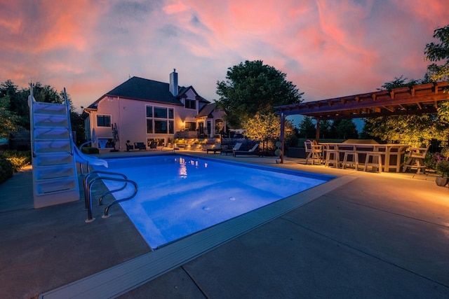 5015 Joshua Dr, West Bend, WI 53090 - pool at dusk with a water slide, an outdoor pool, a patio, and a pergola