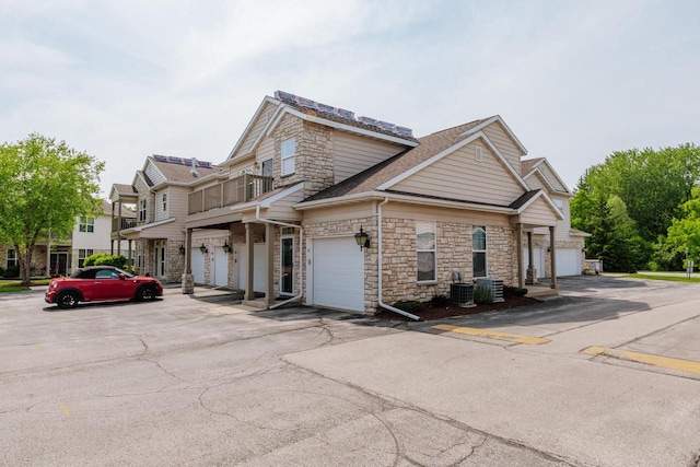 N17W26535 Meadowgrass Cir Unit G, Pewaukee, WI 53072 - view of side of home featuring stone siding, a balcony, central AC, a shingled roof, and a garage