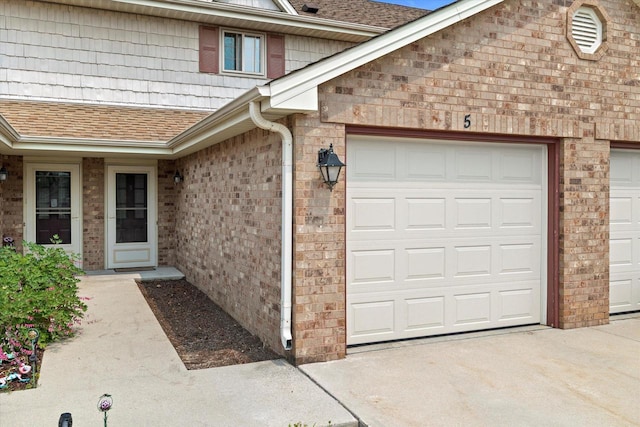 1507 Clarence Ct Unit 5, West Bend, WI 53095 - doorway to property with roof with shingles, an attached garage, brick siding, and concrete driveway