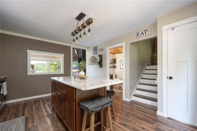 kitchen with a breakfast bar, dark wood finished floors, a center island, baseboards, and hanging light fixtures