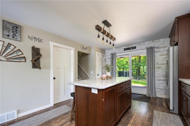 kitchen featuring freestanding refrigerator, light countertops, dark wood-type flooring, a kitchen breakfast bar, and a center island