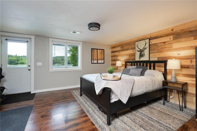 bedroom featuring dark wood finished floors, wood walls, and baseboards