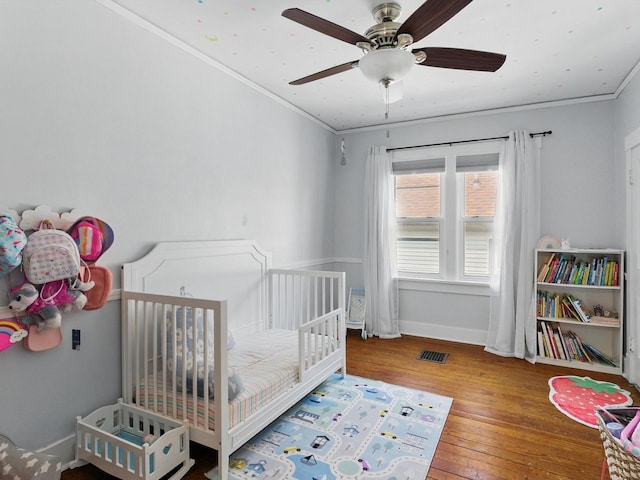 409 Huron St, Manitowoc, WI 54220 - bedroom with wood-type flooring, a crib, ornamental molding, baseboards, and a ceiling fan
