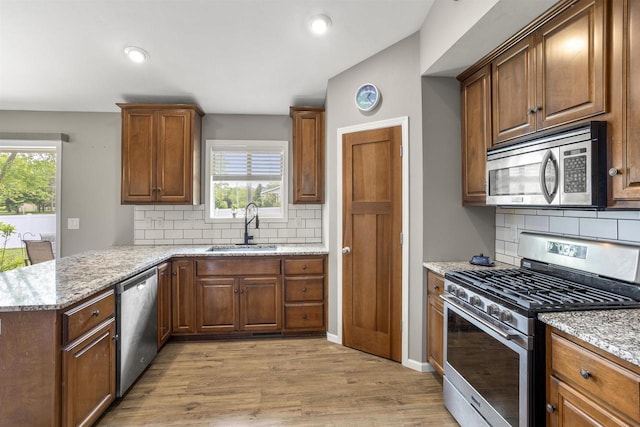 763 Severndroog Way, Howard, WI 54313 - kitchen with appliances with stainless steel finishes, a sink, light wood-type flooring, tasteful backsplash, and light stone countertops