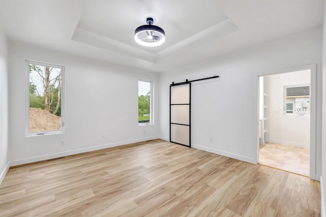 3644 W Hank Ave, De Pere, WI 54115 - unfurnished bedroom with a barn door, a tray ceiling, light wood-style floors, and baseboards