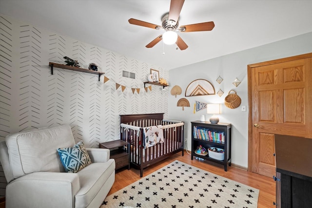 4062 S 106th St, Greenfield, WI 53228 - bedroom with wallpapered walls, light wood-style flooring, a crib, a ceiling fan, and baseboards