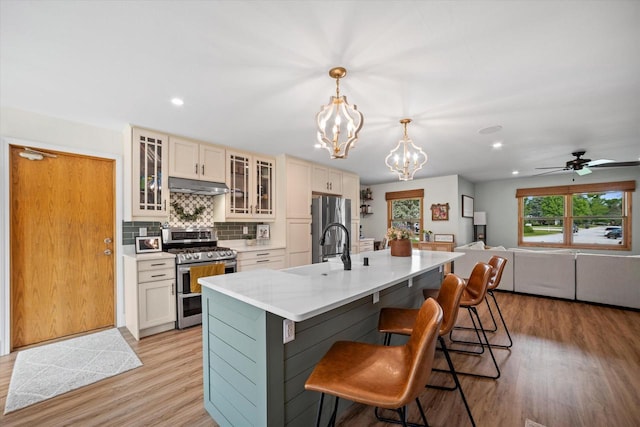 4062 S 106th St, Greenfield, WI 53228 - kitchen featuring stainless steel appliances, under cabinet range hood, a sink, light wood-type flooring, and a kitchen breakfast bar