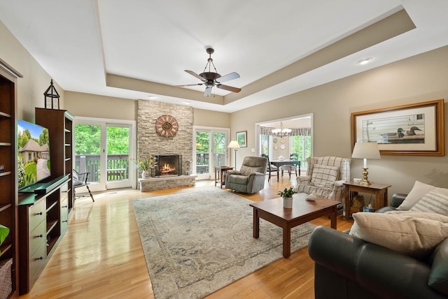 1261 Deer Ct, Lake Geneva, WI 53147 - living area with a raised ceiling, ceiling fan, light wood-style flooring, a stone fireplace, and a chandelier