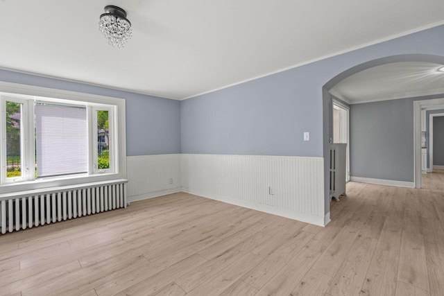 603 Spring St, Lake Geneva, WI 53147 - spare room featuring radiator heating unit, arched walkways, a wainscoted wall, wood finished floors, and ornamental molding