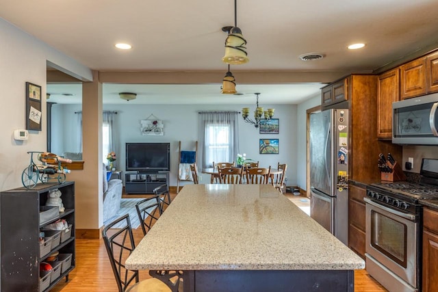 2946 Shadow Ln, Oshkosh, WI 54901 - kitchen with stainless steel appliances, light stone counters, a center island, decorative light fixtures, and light wood-style floors