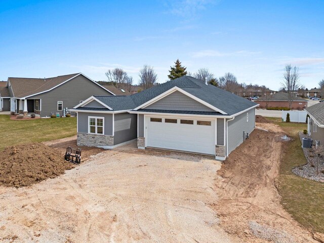 1925 Creekwood Ct, Manitowoc, WI 54220 - view of front of home with stone siding, a garage, driveway, a shingled roof, and central air condition unit