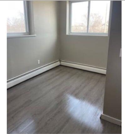 2405 S 5th St, Milwaukee, WI 53207 - spare room with wood finished floors, a baseboard heating unit, and baseboards