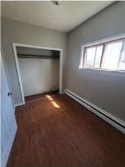 2405 S 5th St, Milwaukee, WI 53207 - unfurnished bedroom featuring baseboard heating, wood finished floors, and a closet