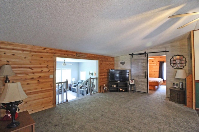 302 Lakeshore Dr, Avoca, WI 53506 - carpeted living room featuring wooden walls, a barn door, ceiling fan, vaulted ceiling, and a textured ceiling