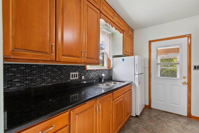 1013 28th St, Two Rivers, WI 54241 - kitchen with a sink, freestanding refrigerator, backsplash, brown cabinetry, and dark stone countertops