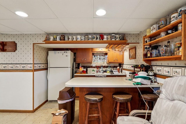 1406 E Oakwood Rd, Oak Creek, WI 53154 - kitchen featuring freestanding refrigerator, wallpapered walls, light countertops, a drop ceiling, and brown cabinetry