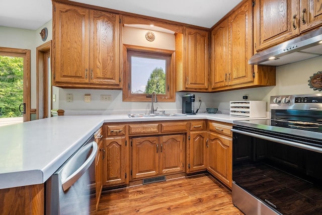 2592 Radinz Rd, Green Bay, WI 54311 - kitchen with appliances with stainless steel finishes, a sink, under cabinet range hood, brown cabinetry, and light wood-style floors