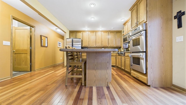N6464 Canterbury Dr, Fond Du Lac, WI 54937 - kitchen with appliances with stainless steel finishes, light wood-type flooring, a breakfast bar, a center island, and baseboards