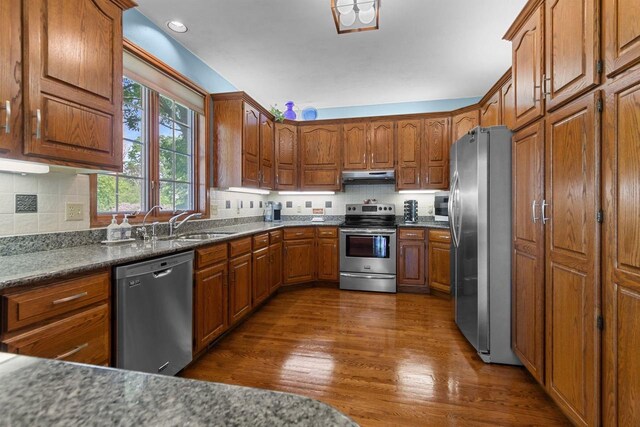 3544 Windsong Ter, Oshkosh, WI 54904 - kitchen featuring stainless steel appliances, under cabinet range hood, brown cabinetry, dark wood-type flooring, and decorative backsplash