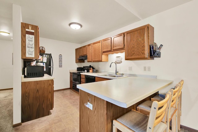 2020 Meadow Ct Unit 2, West Bend, WI 53095 - kitchen featuring black appliances, a sink, under cabinet range hood, light countertops, and brown cabinetry