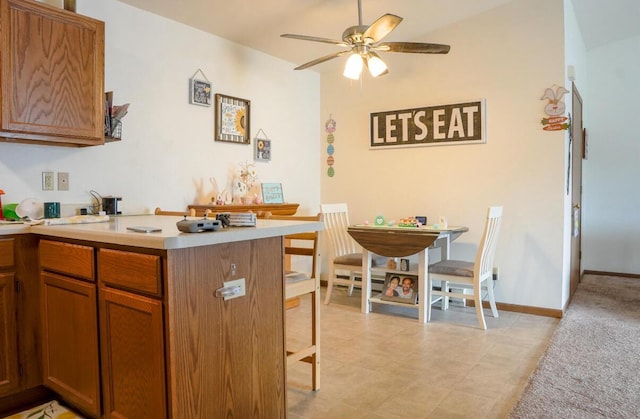 2020 Meadow Ct Unit 2, West Bend, WI 53095 - kitchen with a breakfast bar area, a ceiling fan, brown cabinetry, light countertops, and a peninsula