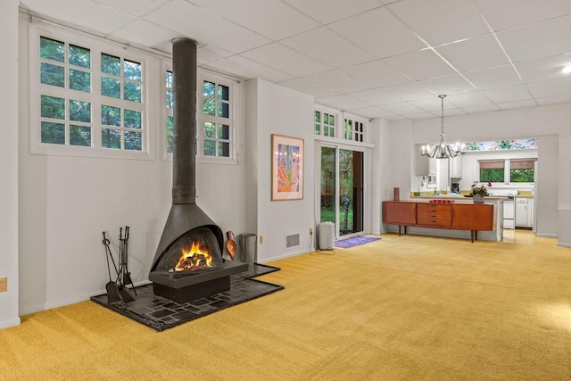 2937 N Mill Rd, Oconomowoc, WI 53066 - living area featuring light colored carpet, a wood stove, a chandelier, a paneled ceiling, and baseboards